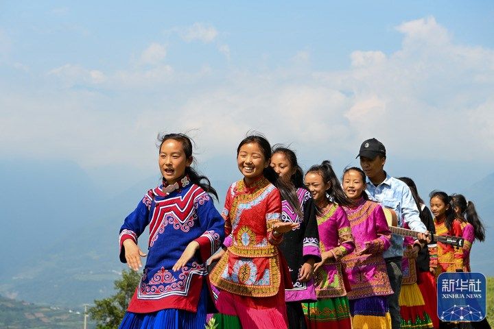 △8月6日，在四川省涼山彝族自治州普格縣大槽鄉(xiāng)，妞妞們和吉布小龍在戶外唱歌。在彝族家庭里，父母一般把女兒喚作“妞妞”。在位于四川省涼山彝族自治州普格縣的大槽鄉(xiāng)中心小學，有一個全是由妞妞組成的童聲合唱團——妞妞合唱團。2018年的一個課間，老師吉布小龍抱著吉他坐在操場邊輕聲彈唱。幾個女孩循著歌聲圍坐了過來，跟著音樂一起小聲哼唱?！澳銈兿氤鑶?？”吉布小龍問到。女孩們沒有說話，眨著眼睛，怯生生地點點頭。在小龍老師的鼓勵下，音樂教室里的妞妞漸漸多了起來。通過在抖音等短視頻平臺上的創(chuàng)作分享，吉布小龍讓更多人看到了妞妞合唱團。2021年夏天，妞妞合唱團接到邀請，去北京參加了音樂節(jié)。妞妞們唱著歌走出大山，走向更大的舞臺。